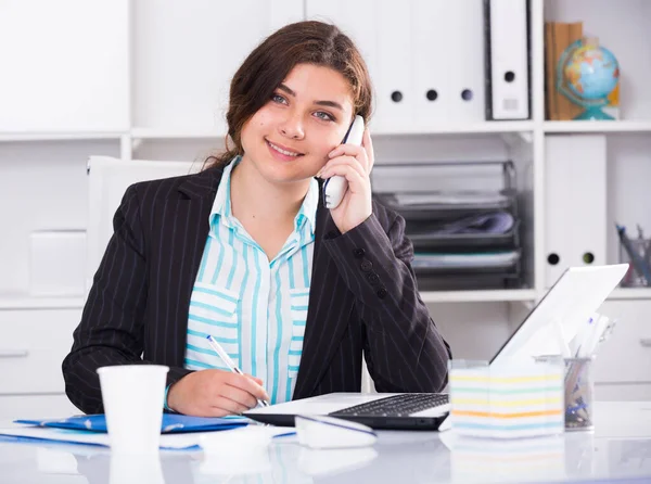 Young woman is working at a computer and talking phone — Stock Photo, Image