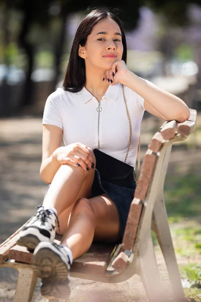 Aantrekkelijk Braziliaans meisje zittend op een bankje in zomerpark — Stockfoto