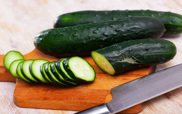 Cut fresh cucumbers on wooden table in home kitchen — Stock Photo, Image