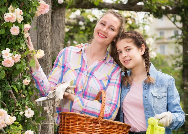 Fena s dlouhými kudrnatými vlasy a dívka stojící v blízkosti růží květiny venku — Stock fotografie