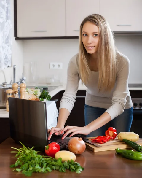 Donna che utilizza notebook durante la cottura di verdure — Foto Stock