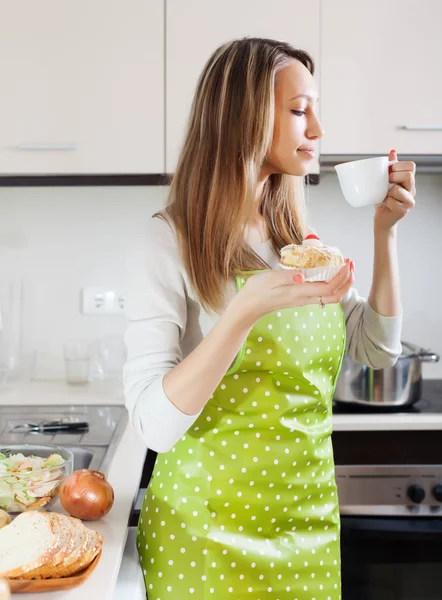 Mujer en delantal bebiendo té con pastel — Foto de Stock