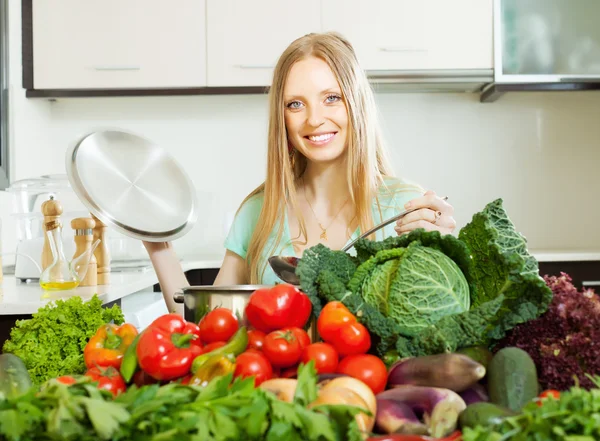 Blonde femme aux cheveux longs cuisine avec des légumes — Photo