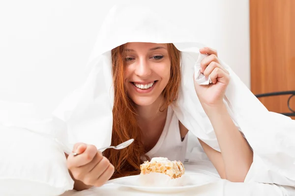 Vrouw eten zoete taart onder blad in bed — Stockfoto