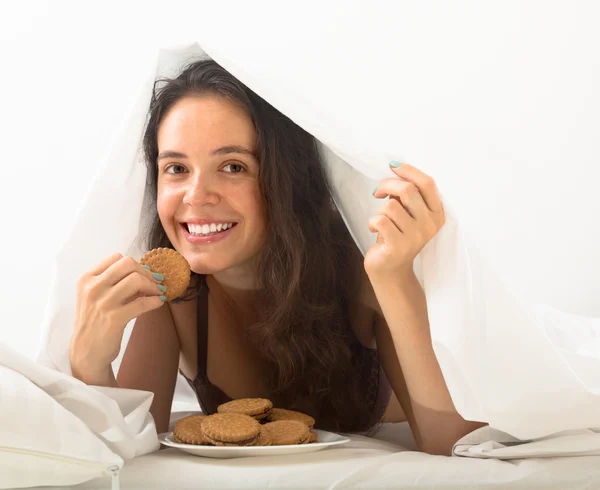 Mädchen isst Kekse im Bett — Stockfoto
