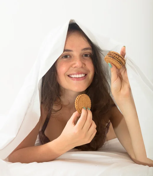 Dívku jíst cukroví v posteli — Stock fotografie