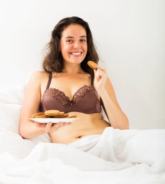 Woman eating cookies in bed — Stock Photo, Image