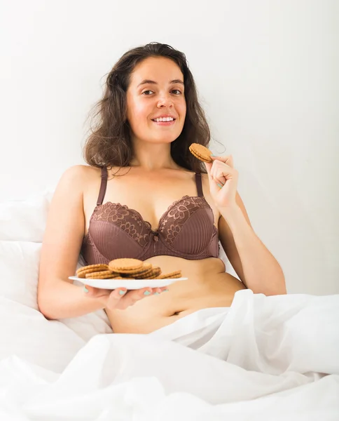 Κορίτσι τρώει μπισκότα στο κρεβάτι — 图库照片