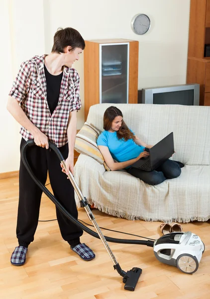 Guy doing house cleaning during girl resting — Stock Photo, Image