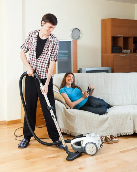 Man reiniging met stofzuiger terwijl vrouw liggen met ebook — Stockfoto