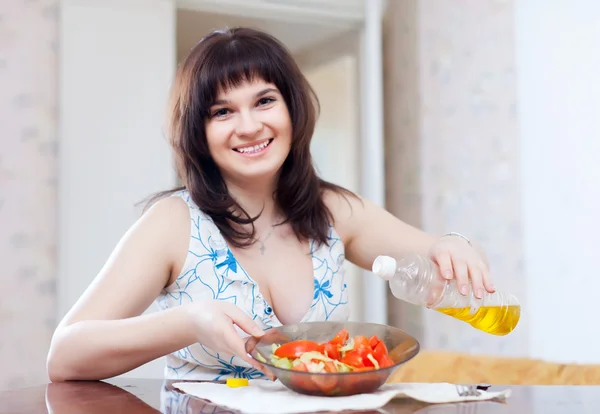 Positive woman pours oil to vegetables salad — Stock Photo, Image