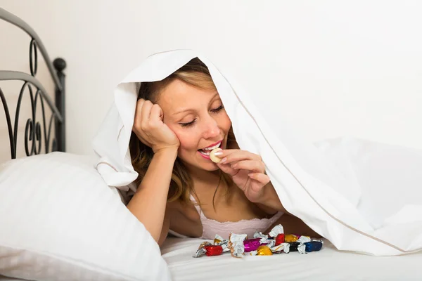 Woman secretly eating candy in bed — Stock Photo, Image