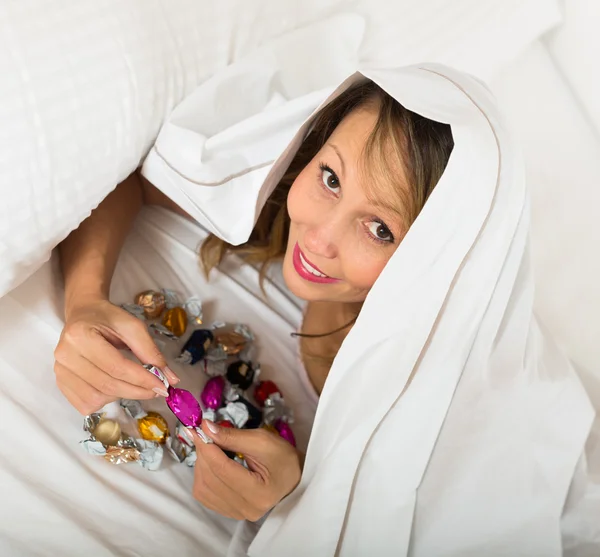 Frau isst heimlich Süßigkeiten im Bett — Stockfoto