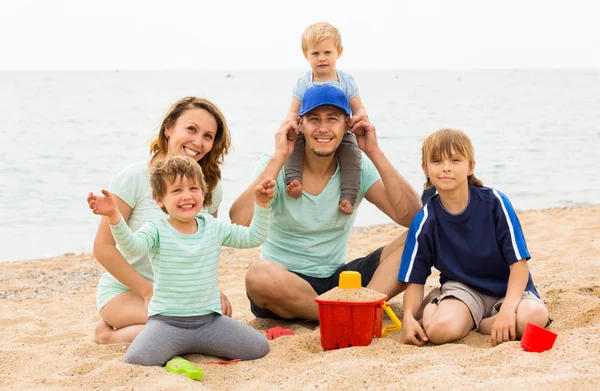 Positive parents with kids sitting at sandy beach — Stock Photo, Image
