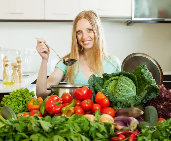 Långhåriga kvinna matlagning med högen av råa grönsaker — Stockfoto