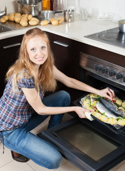 Cheeful 女人烹饪烤箱里的生鱼 — 图库照片