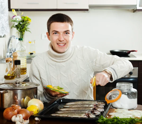 Happy man cooking raw fish with lemon in roasting pan — Stock Photo, Image