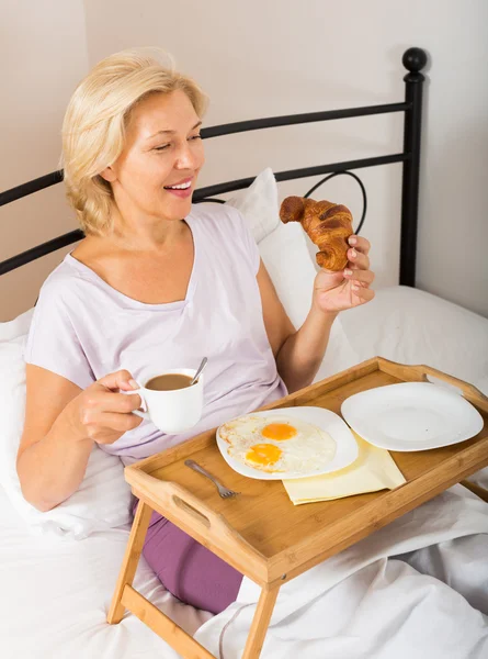 성숙 한 여자가 침대에서 아침 식사를 즐긴다 — 스톡 사진