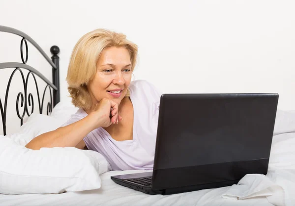 Donna matura con computer portatile a letto — Foto Stock