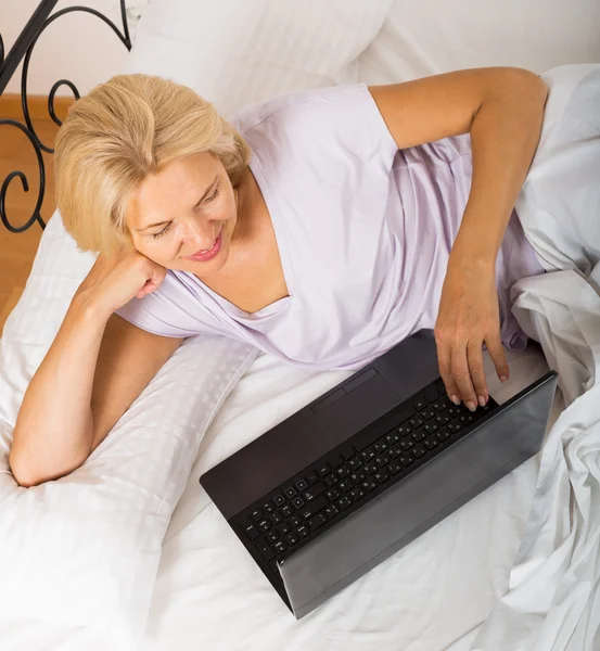 Donna matura con computer portatile a letto — Foto Stock