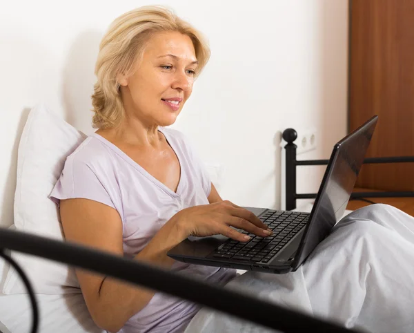 Mulher madura com laptop na cama — Fotografia de Stock