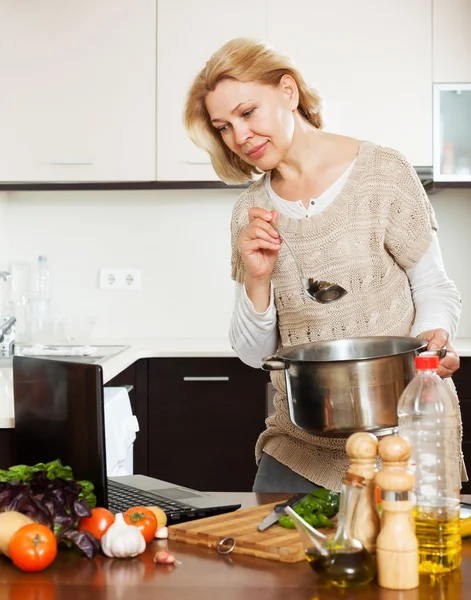 Kvinna som använder bärbar dator under matlagning — Stockfoto