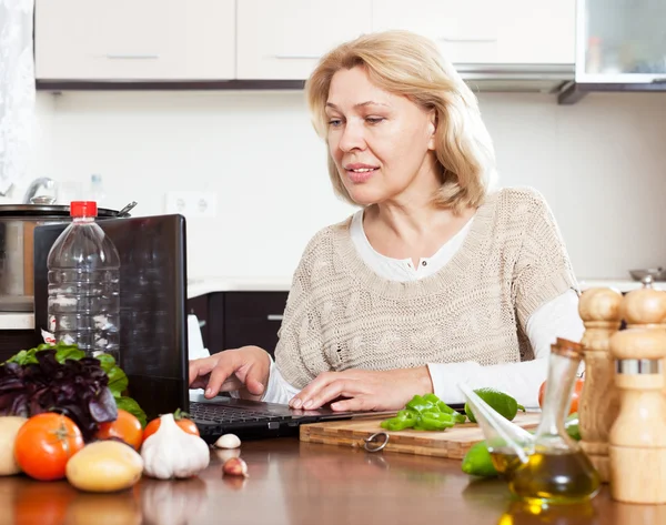 Femme au foyer mature avec ordinateur portable dans la cuisine — Photo