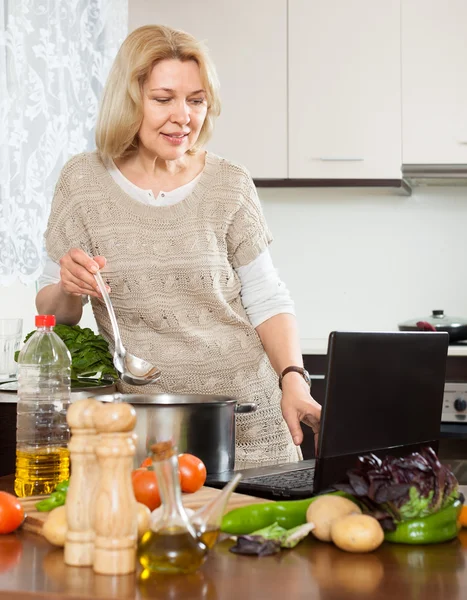 Hemmafru använder bärbar dator medan matlagning — Stockfoto