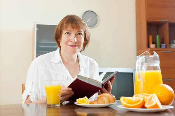 Mulher madura tomando café da manhã com livro — Fotografia de Stock