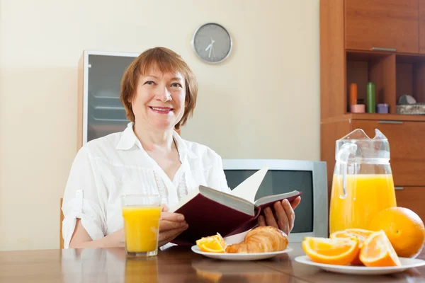 Mogen kvinna äter frukost med bok — Stockfoto