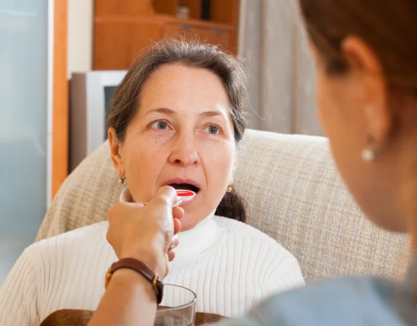 Woman giving  syrup to mature mother — Stock Photo, Image