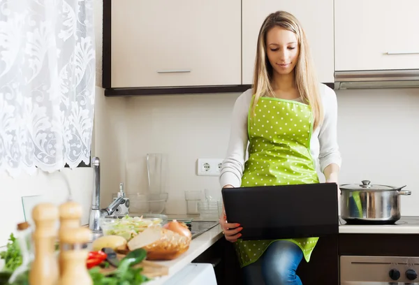 Flicka i förkläde matlagning med bärbar dator — Stockfoto