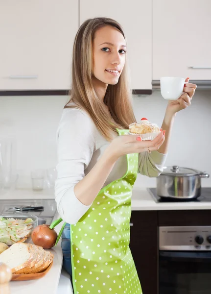 Frau in Schürze isst Kuchen mit Tee — Stockfoto