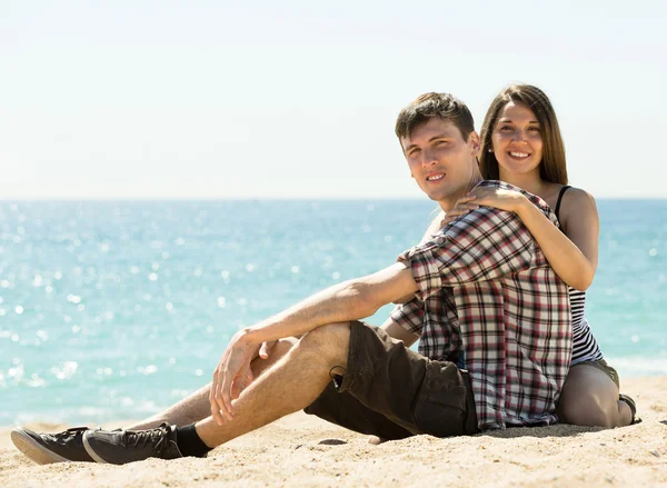 Улыбающаяся пара сидит на песке — стоковое фото