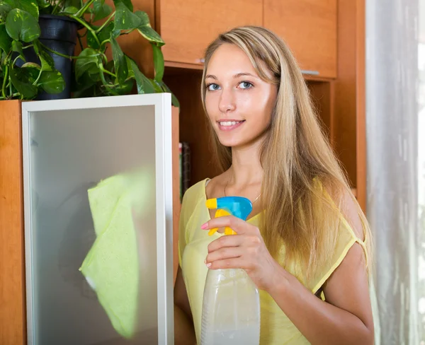 Blond meisje schoonmaken glazen deur van meubilair — Stockfoto