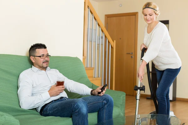 Frau staubsaugt Zimmer, Mann entspannt — Stockfoto