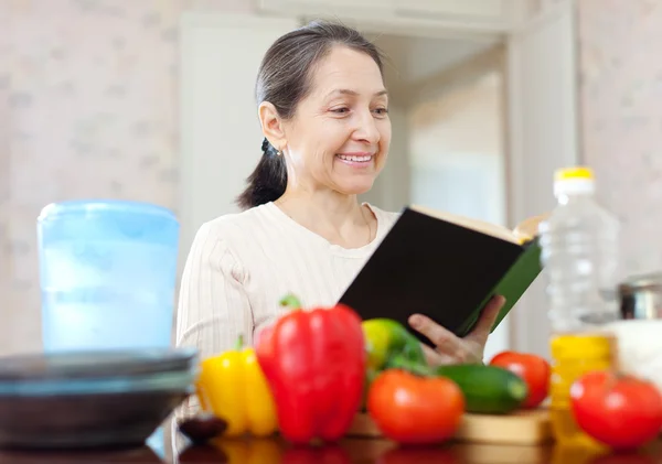 Mujer madura lee libro de cocina —  Fotos de Stock