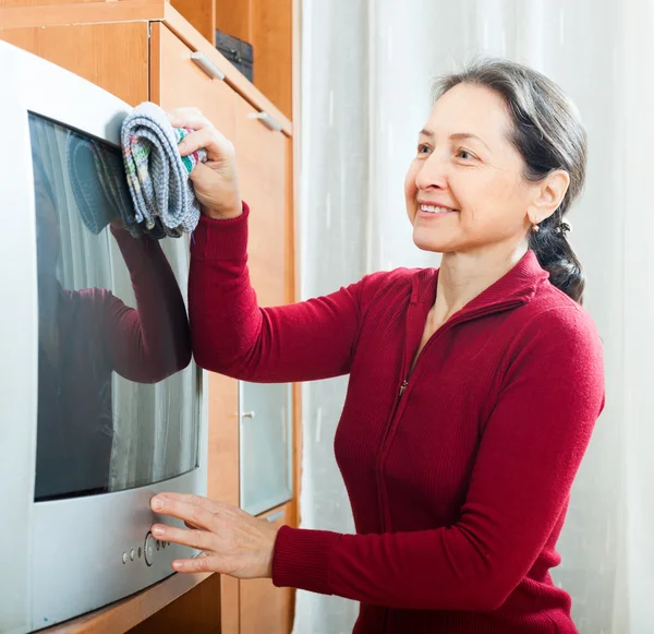 Lächelnde reife Frau staubt Fernseher ab — Stockfoto