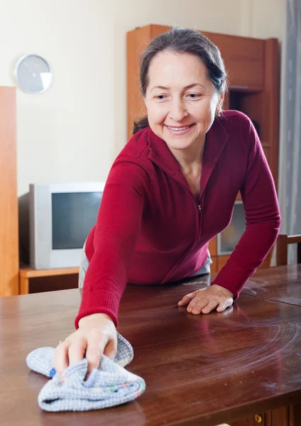 Reife Frau putzt Tisch mit Lappen — Stockfoto