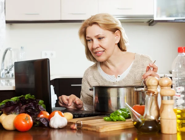 Hemmafru använder bärbar dator medan matlagning — Stockfoto