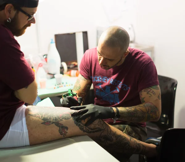 Художник делает татуировку на ноге клиента — стоковое фото