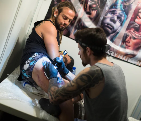 Konstnär som gör tatueringen på manlig klient ben — Stockfoto