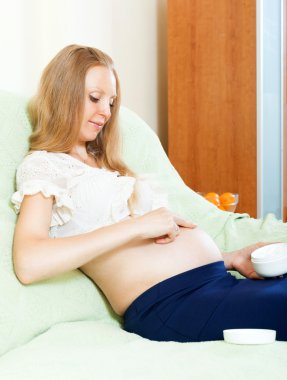 Pregnant woman putting cream on stomach clipart