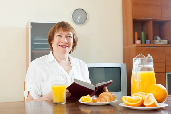Mulher madura tomando café da manhã com livro — Fotografia de Stock