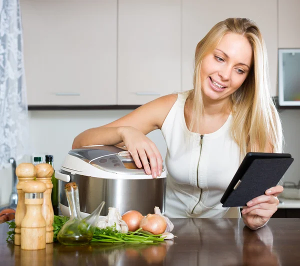 Femeie citind ereader lângă multicooker — Fotografie, imagine de stoc