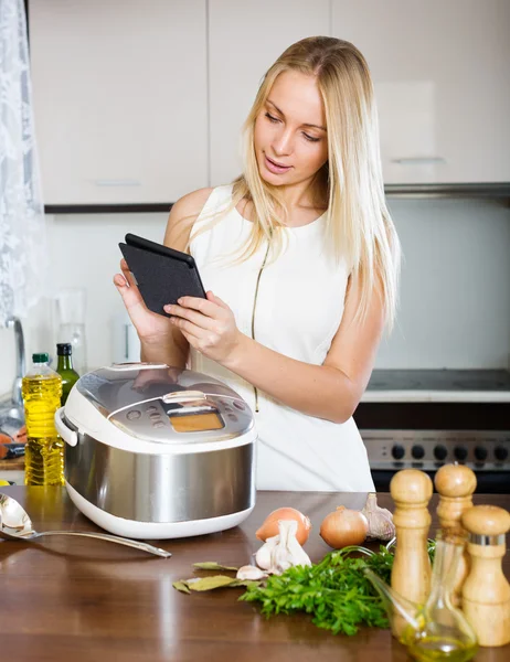 Housewife reading ereader and cooking — Stock Photo, Image
