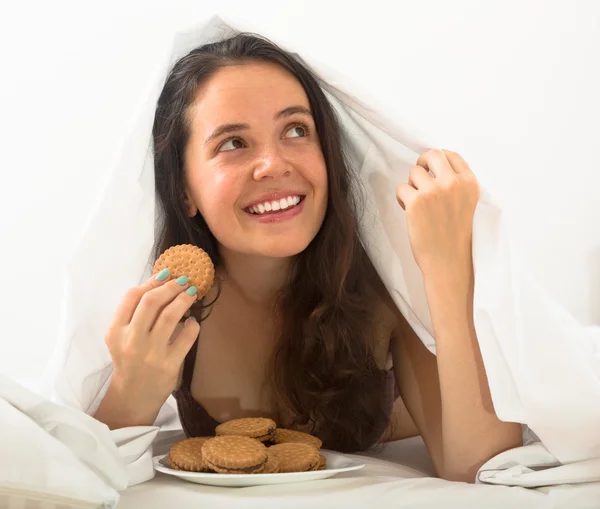 Mädchen isst Kekse im Bett — Stockfoto
