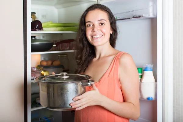 Голодная девушка с кастрюлей возле холодильника — стоковое фото