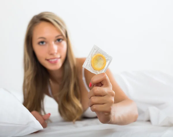 Mujer sexy sosteniendo condón en la cama — Foto de Stock