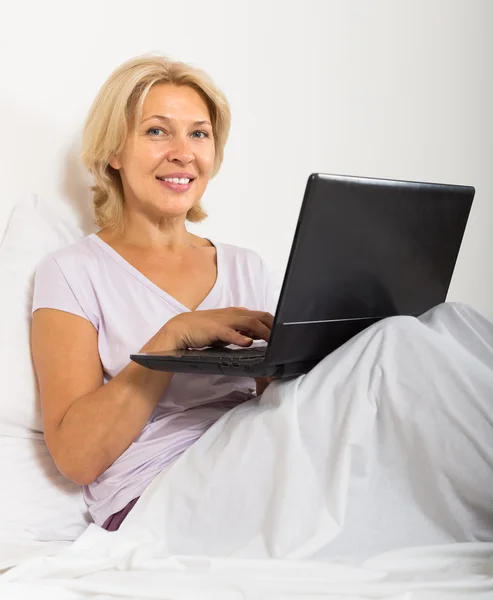 Mujer madura con portátil en la cama — Foto de Stock
